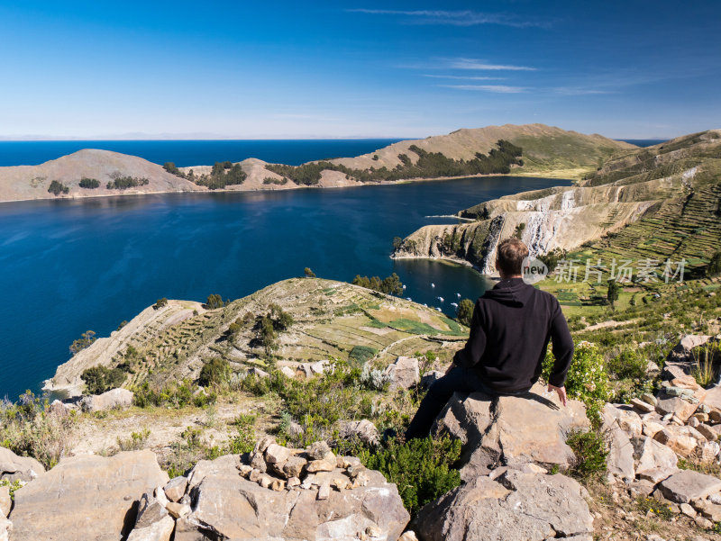 玻利维亚科帕卡巴纳，阳光岛，titicaca isla del sol湖，年轻的白人男性坐在欣赏美丽的风景山丘，山脉